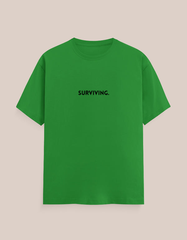 Green t-shirt with 'SURVIVING.' text on a beige background