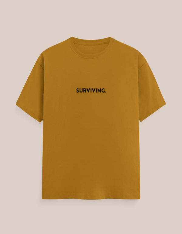 Mustard yellow t-shirt with 'SURVIVING.' text on a beige background
