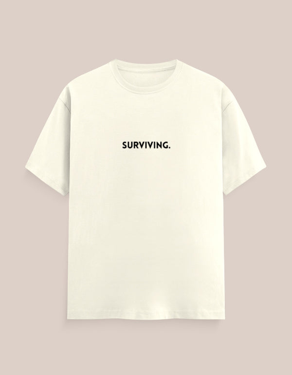 White t-shirt with 'SURVIVING.' text on a light pink background
